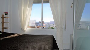 Un dormitorio con cama, ventana con cortinas, vista a edificios y un radiador.