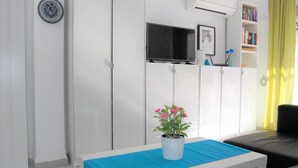 Una sala de estar moderna con un sofá blanco, una mesa azul con una planta en maceta y un televisor sobre un mueble.