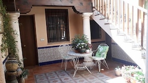 Ein überdachter Patio-Bereich mit einem runden Tisch und zwei Stühlen, umgeben von Topfpflanzen.