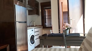 Eine kompakte Küche mit Kühlschrank, Mikrowelle und Waschmaschine. Es gibt eine Essecke mit Tisch und Stühlen sowie ein Fenster mit Ausblick.