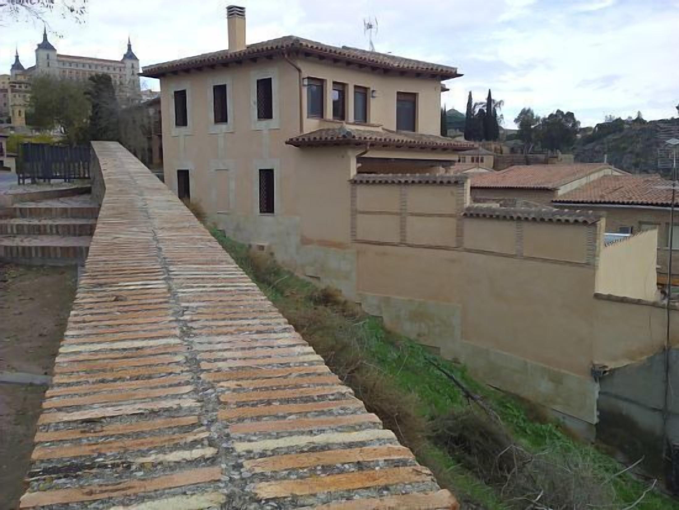 A stone pathway leading to a building with a tiled roof and multiple windows.