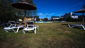 A poolside area with lounge chairs and umbrellas, a swimming pool, and buildings in the background.