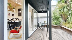 A wooden deck with a table and chairs, a red chair, and a small table with a plant. - Aspen Studio (Christchurch)
