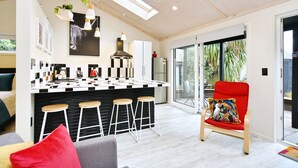 A modern kitchen with a central island, bar stools, and a red chair with a colorful cushion. - Aspen Studio (Christchurch)