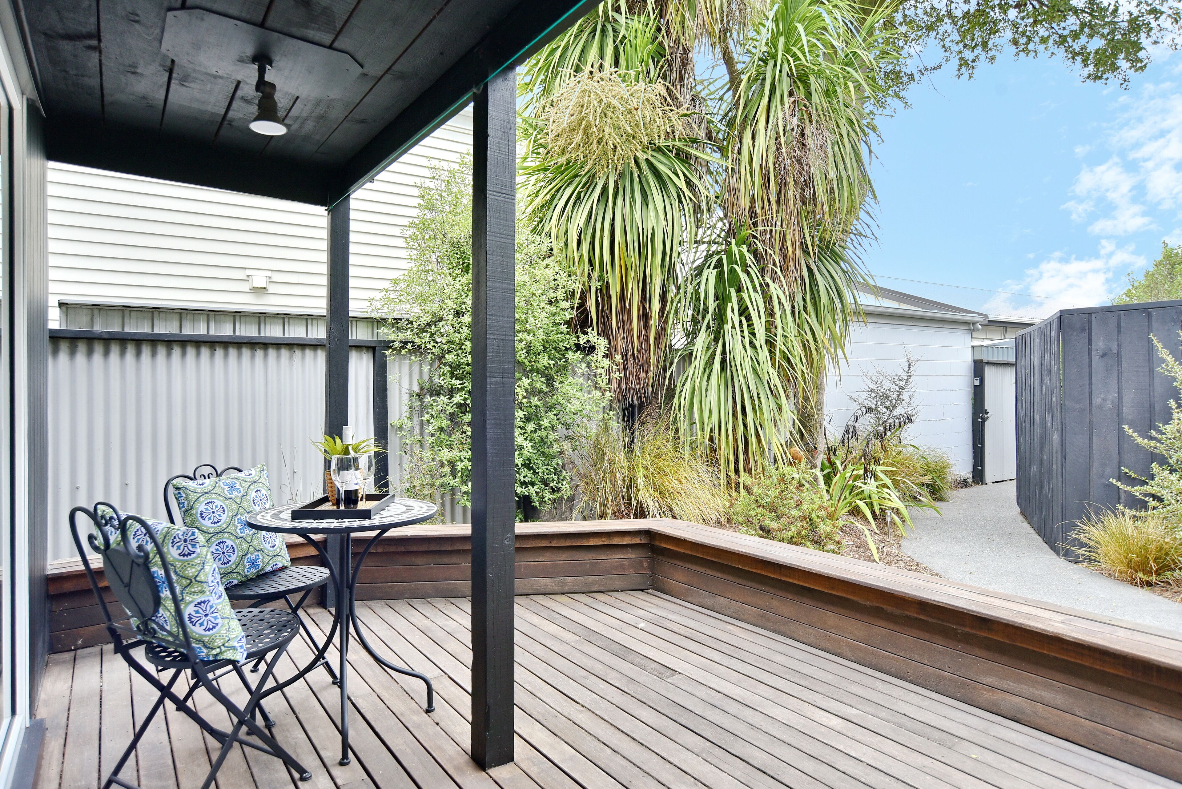 A wooden deck with a table and chairs, surrounded by plants and a fence.