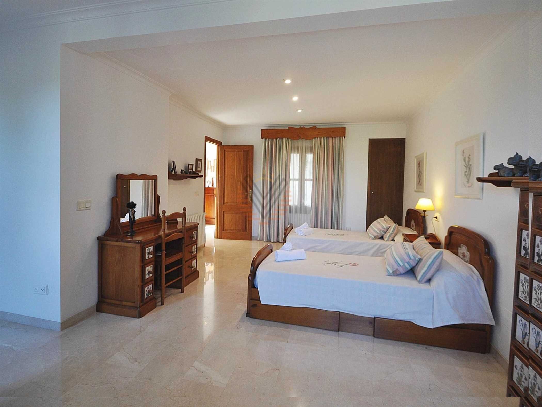 Quarto com duas camas, um penteou, um espelho e uma porta que dá para outro cômodo.