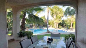 A glass-top table with chairs, a hat, and a metal cup, overlooking a pool with palm trees and lounge chairs. - Can Gual de Inca, Elegant Vila, Mallorca (Inca)