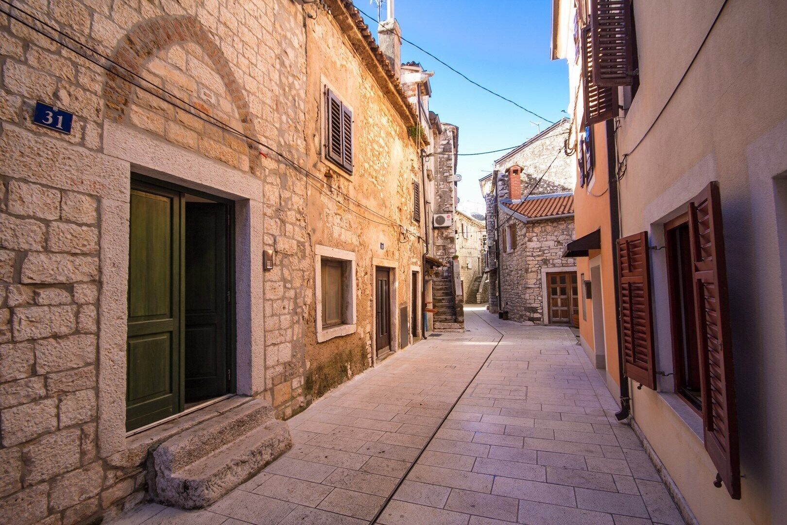 A narrow stone-paved street flanked by historic buildings with wooden shutters and stone facades.