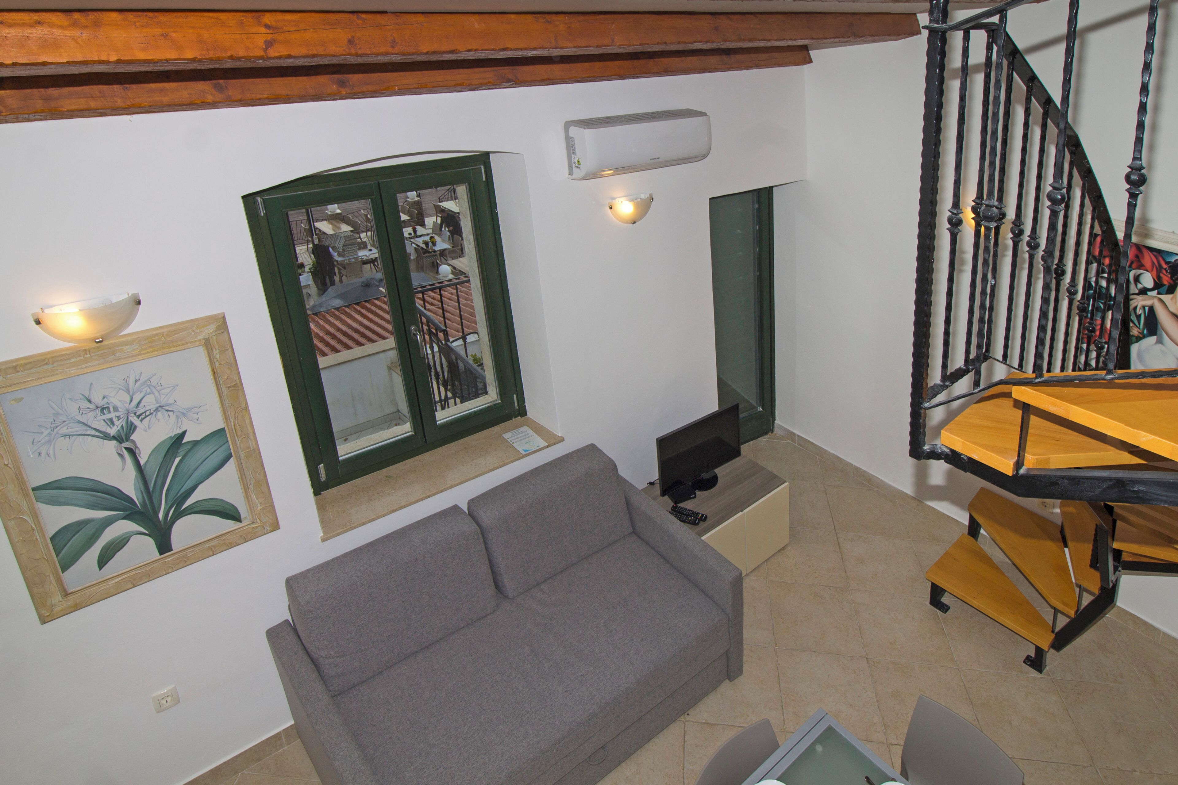 Un salon comprenant un canapé, un téléviseur, un escalier et une fenêtre donnant sur l’extérieur.