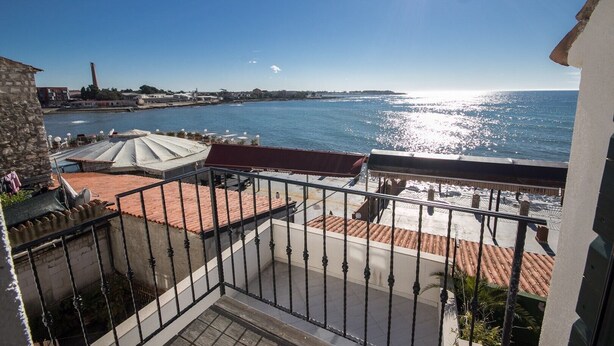 Een balkon met uitzicht op zee, een stenen gebouw en een dak met rode tegels.