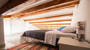 Een slaapkamer met een bed, een nachtkastje, een lamp, een kleurrijk vloerkleed en een houten plafond.