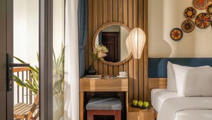 Habitación de hotel con escritorio de madera, espejo, mesita de noche con lámpara, cama y vistas al balcón exterior.