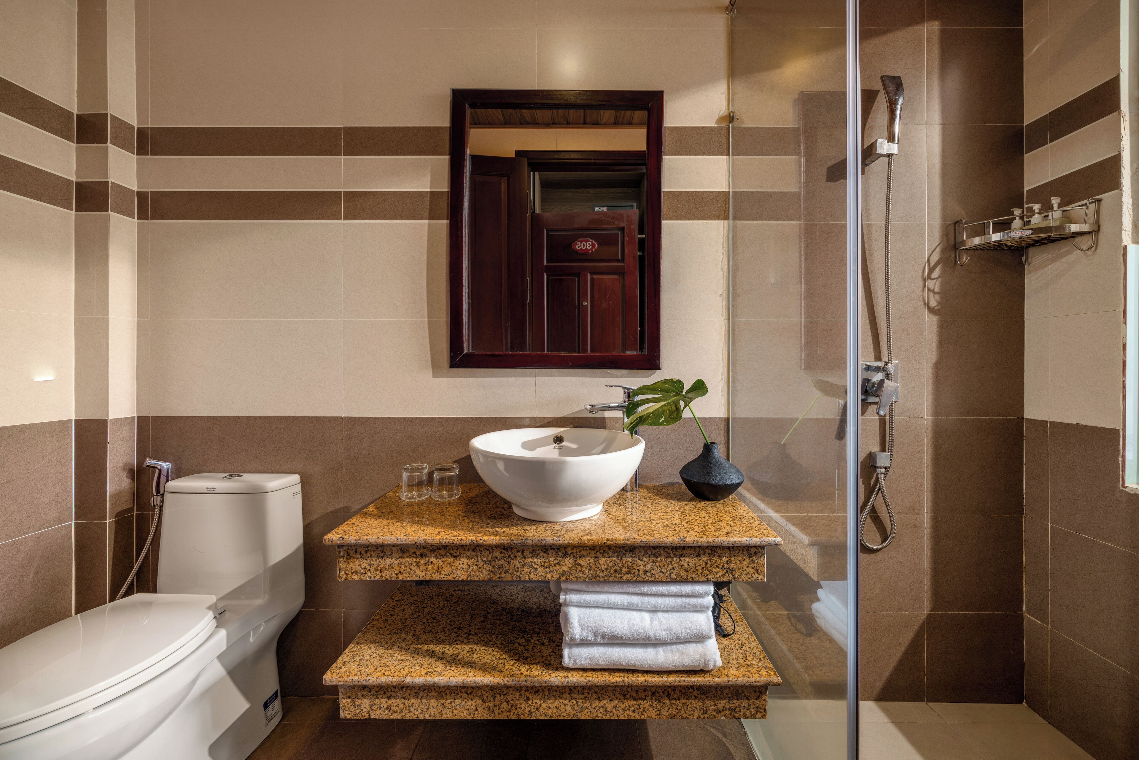 Une salle de bain avec des toilettes blanches, un lavabo à grande cuve, un miroir et un espace douche.