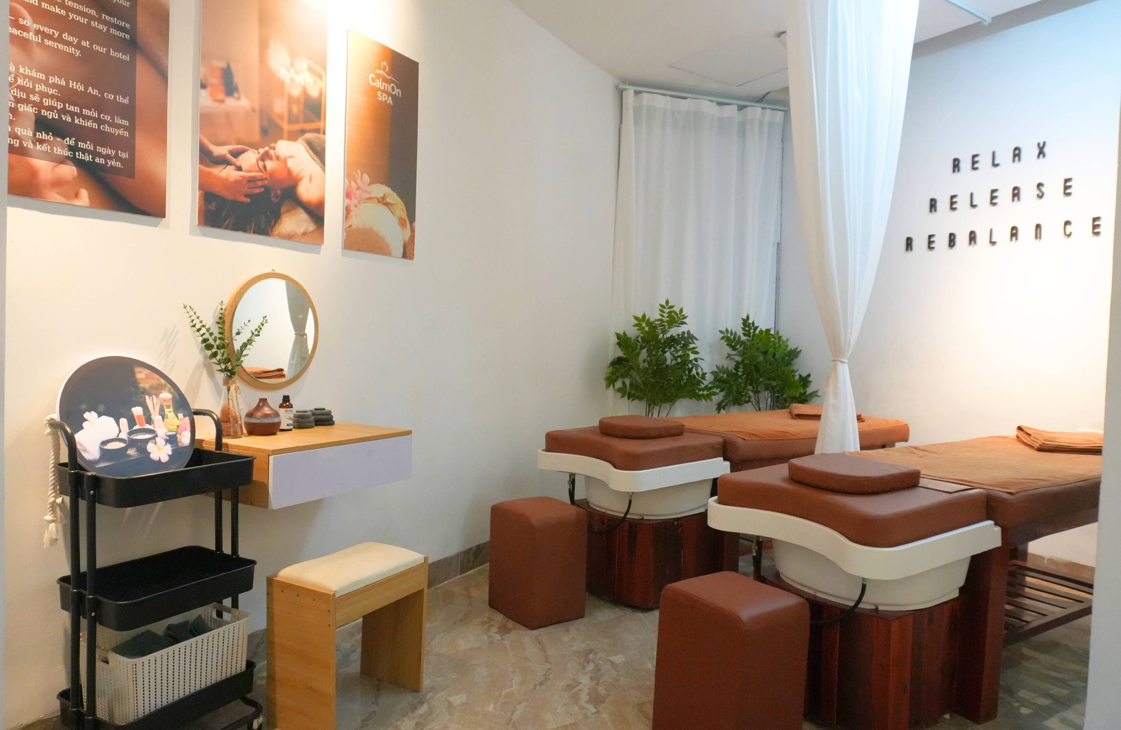 Une salle de spa équipée de tables de massage, d’un petit banc en bois, d’un miroir et de quelques affiches accrochées au mur.