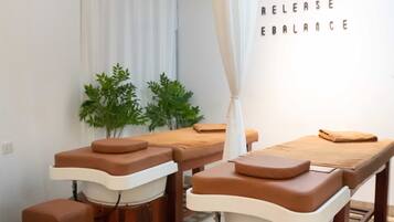 A massage therapy room with wooden tables and brown cushions, a white curtain, and a wall with the words "RELAX RELEASE EBALANCE".
