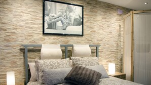 A bedroom with a stone wall, a framed picture, a bed with patterned bedding, and bedside lamps.