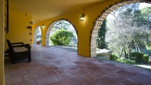 A covered patio with stone arches, yellow walls, and a view of greenery.