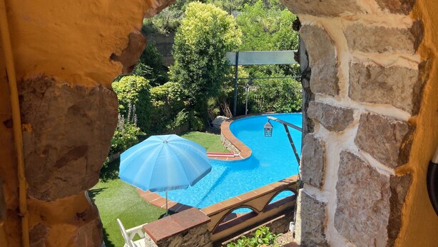 A stone-walled pool area with a blue pool, a white umbrella, and a wooden deck.