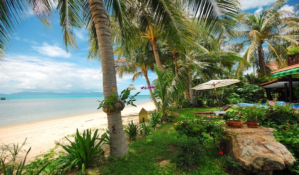 A beach with palm trees, a lounge area with umbrellas, and a view of the sea.
