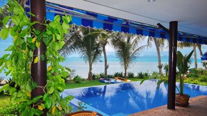 A pool area with a view of the sea, surrounded by palm trees and a blue awning. - Superb Beachfront Villa with private Pool & Jacuzzi in tropical garden. (Ko Samui)