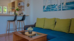 Una sala de estar moderna con un sofá azul, cojines verdes, una mesa de centro de madera y un cuadro de veleros en la pared.