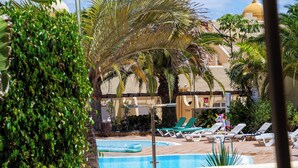 A poolside area with lounge chairs, a pool, and a palm tree. - 3 bedroom villa in sultan complex with wifi/UKTV/pools (Corralejo)