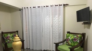 Un salón con dos sillas de madera con cojines estampados, una mesita, un jarrón decorativo y una cortina de diseño geométrico.