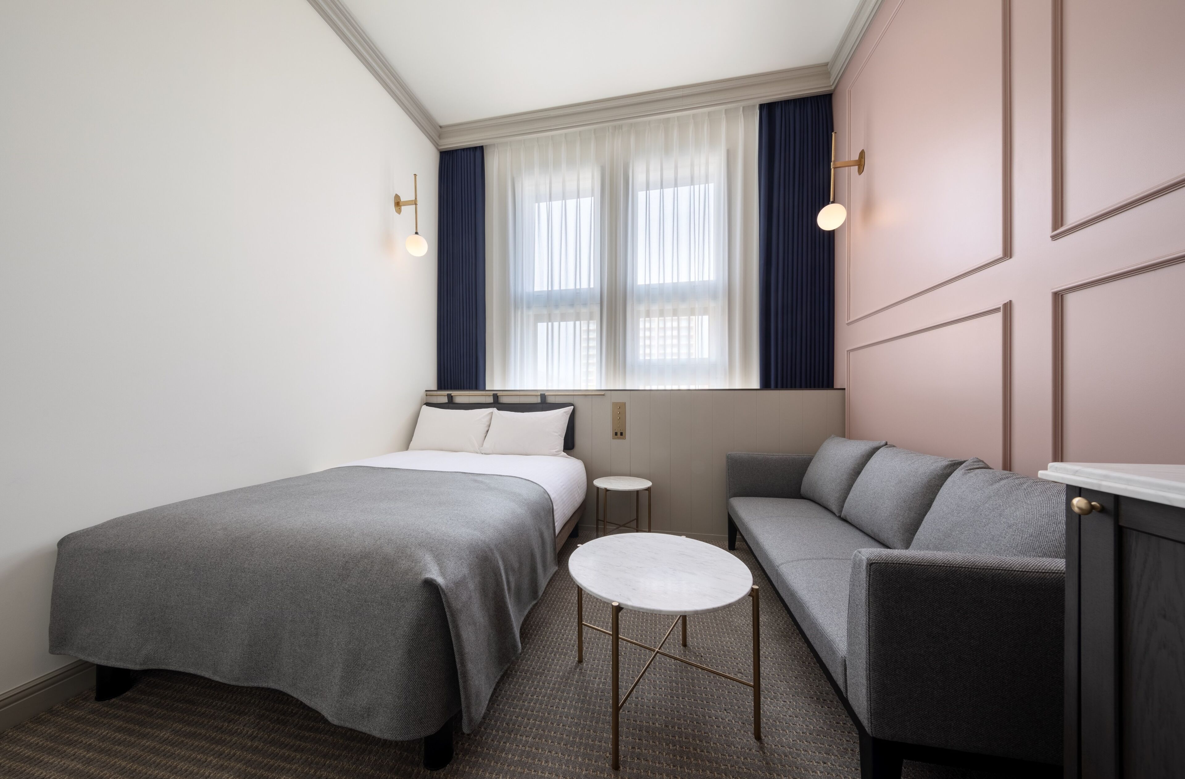 A hotel room with a bed, a sofa, a small round table, and a window with curtains.