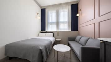 A hotel room with a bed, a sofa, a small round table, and a window with curtains.