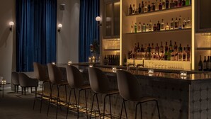 A bar area with a long counter, multiple stools, and shelves stocked with bottles and glasses.