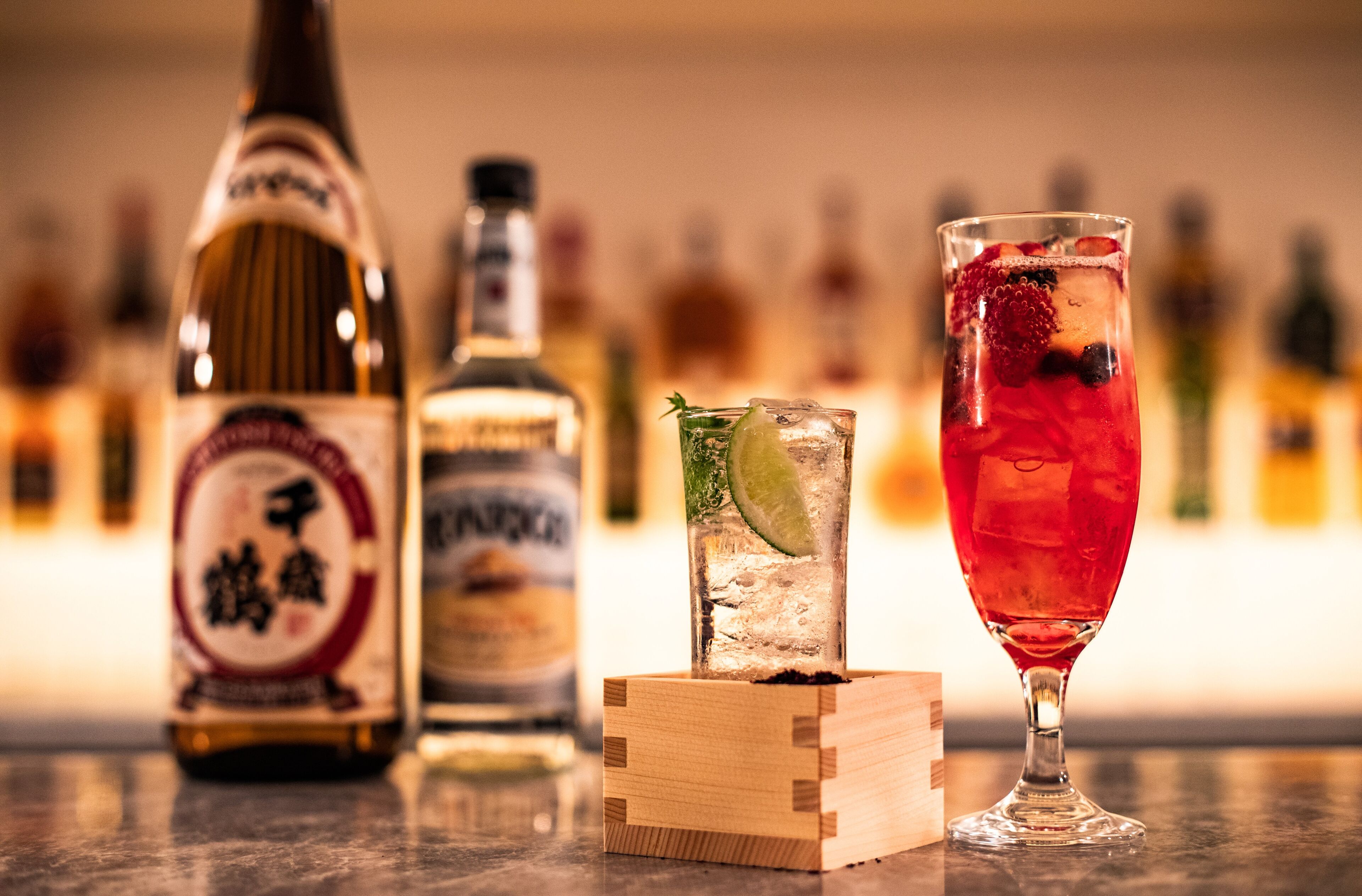 A bar setting with a bottle of liquor, a glass with a red drink, and a lime wedge.