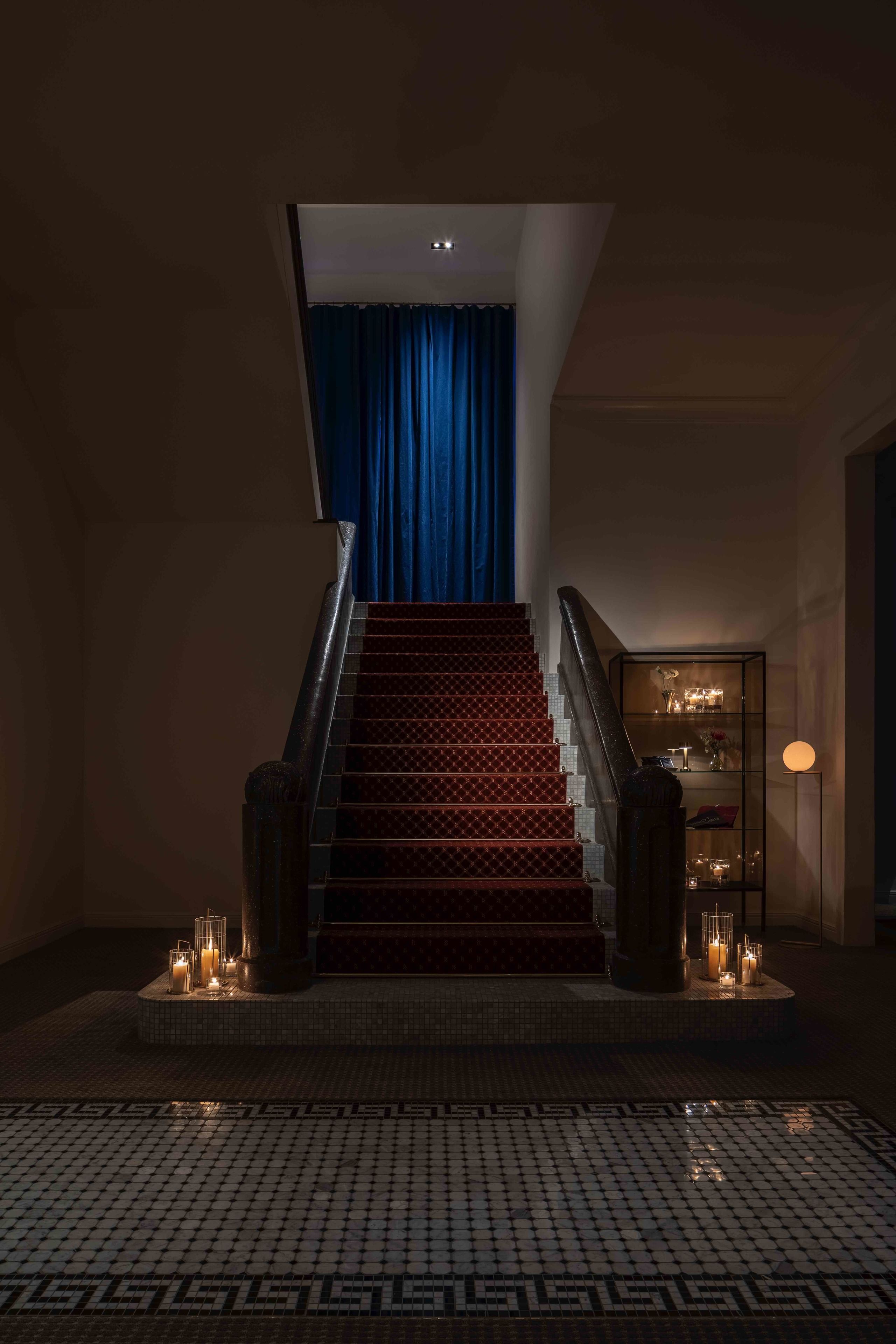 A staircase with a red carpet, a blue curtain at the top, and a tiled floor with a geometric pattern.