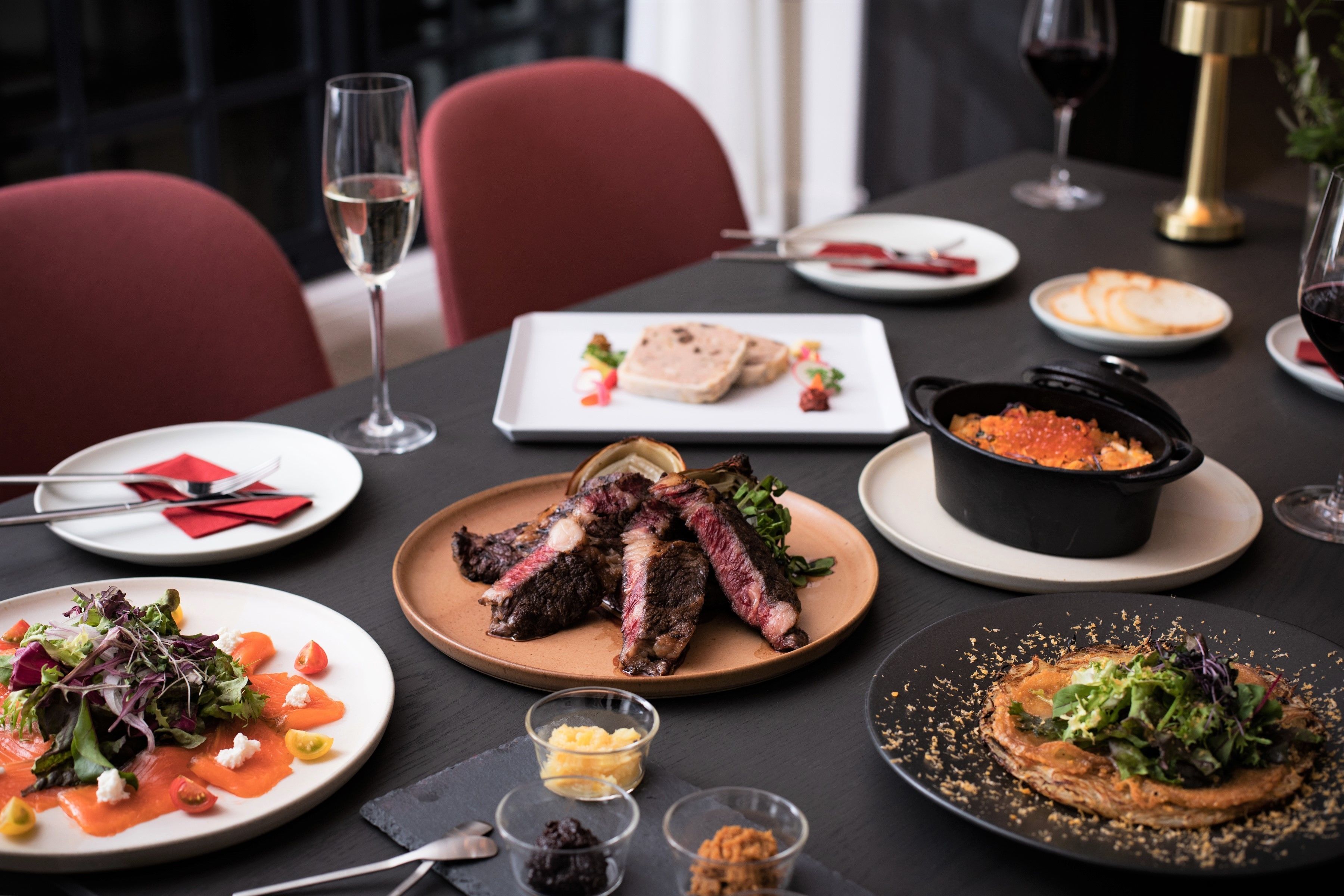 A dining table set with various dishes, including steak, salad, and a pot of red caviar.