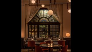 A dining area with a large stained glass window, multiple hanging spherical lights, and a cozy seating arrangement.