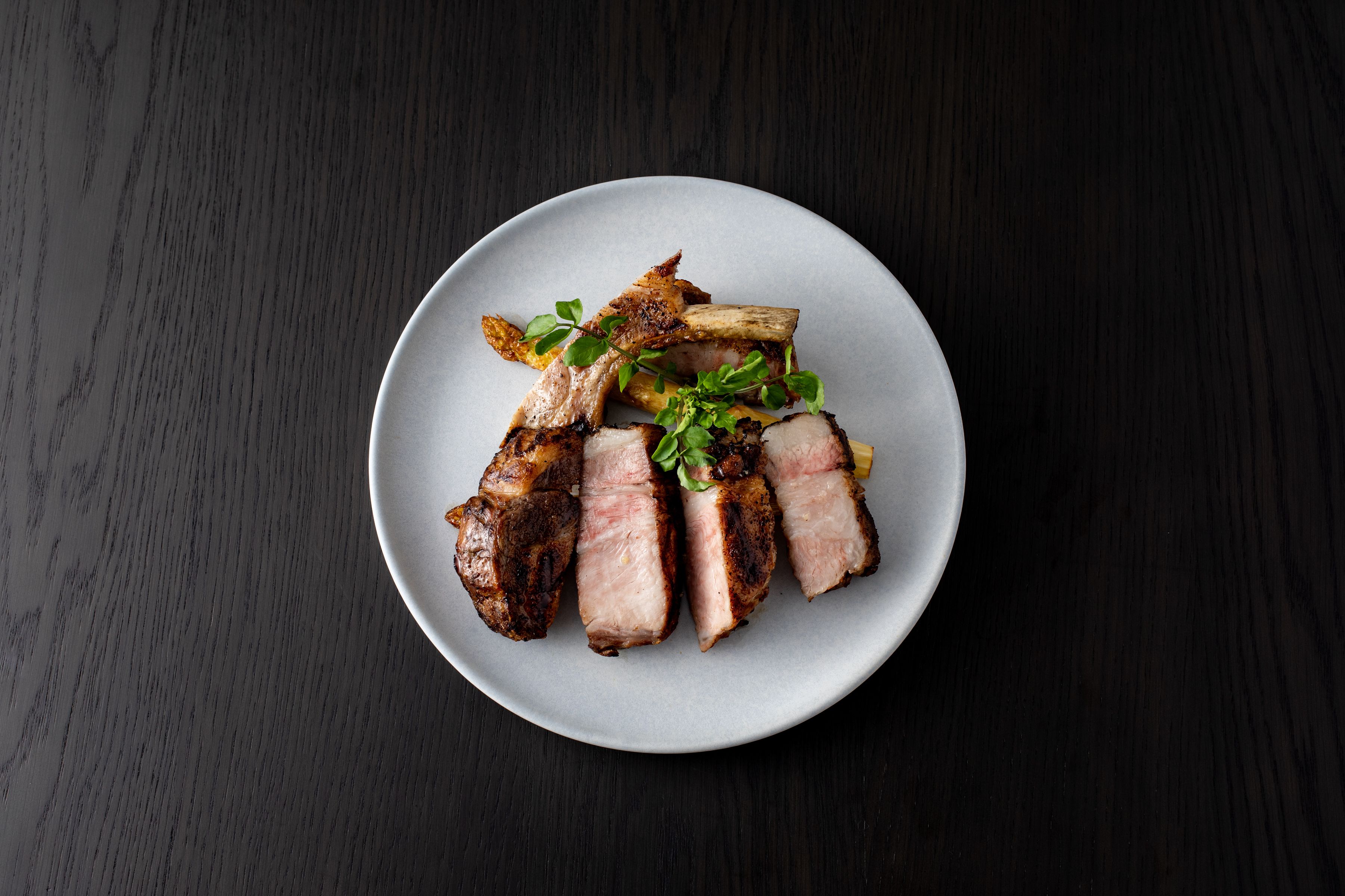 A plate of sliced meat with vegetables on a dark wooden table.