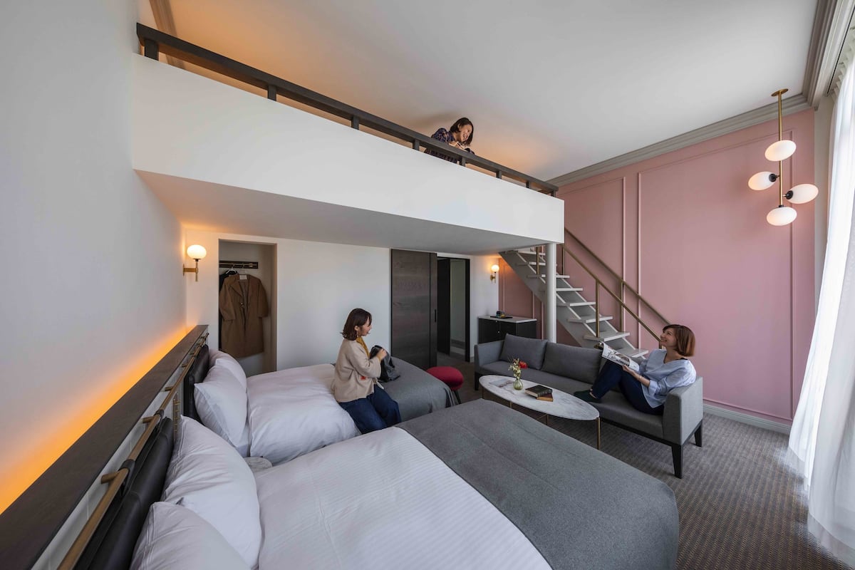 Ett modernt hotellrum med en våningssäng, en soffa, ett litet bord och en trappa som leder upp till en övre våning.