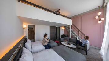 Una habitación de hotel moderna con una cama entrepiso, un sofá, una pequeña mesa y una escalera que lleva a un nivel superior.