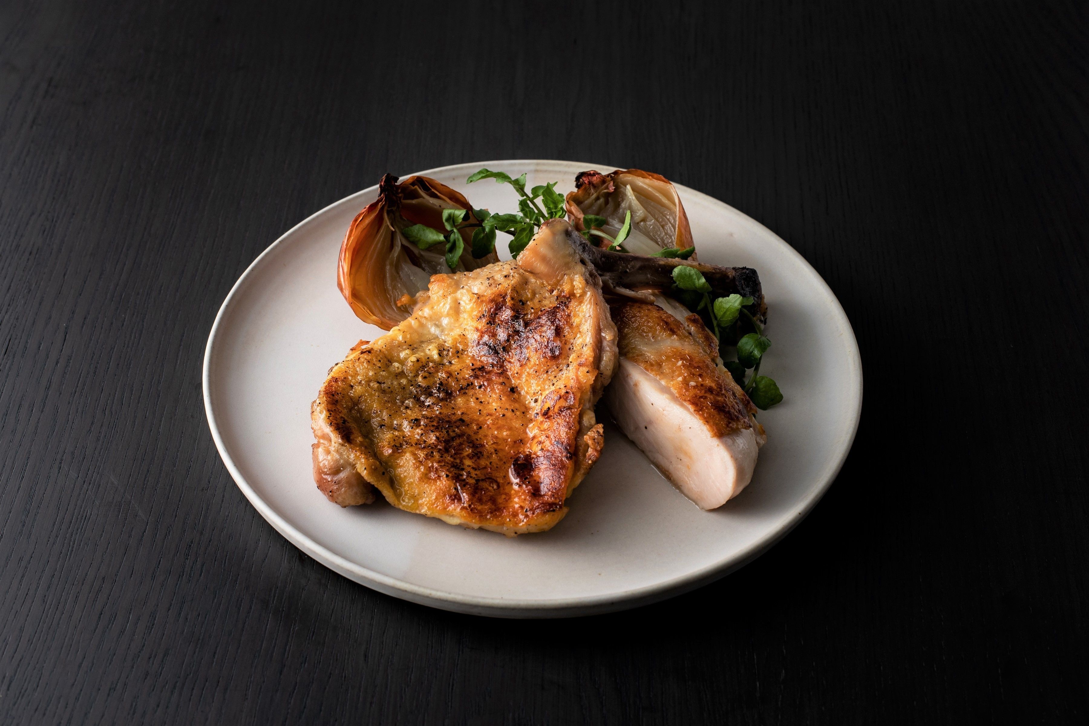 Prato com frango grelhado e uma concha de marisco em superfície escura.