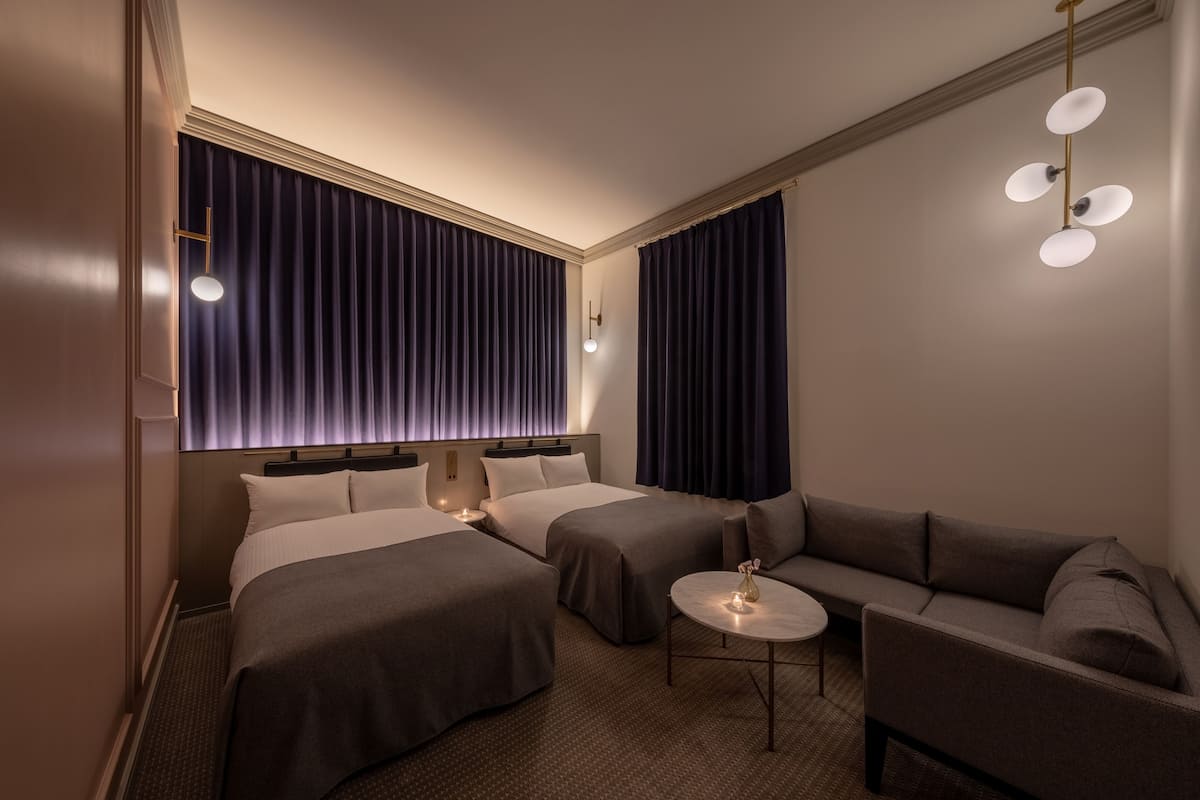 Ett hotellrum med två sängar, en soffa, ett litet bord och en taklampa.