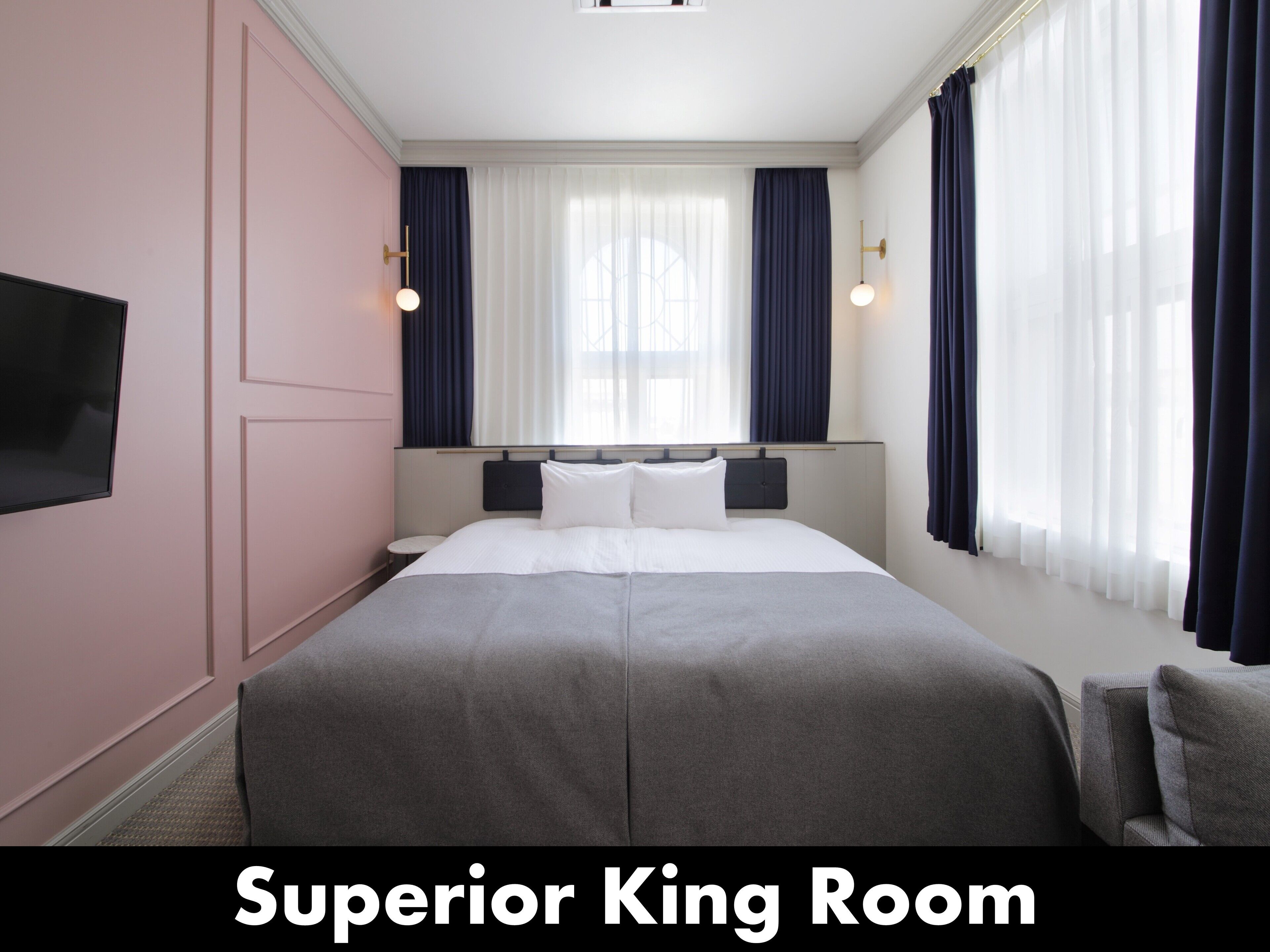 Ein Hotelzimmer mit einem Bett, einem an der Wand befestigten Fernseher und Vorhängen an den Fenstern.