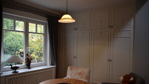 A room with a round wooden table, a chair with floral upholstery, a window with curtains, a radiator, and a wardrobe with multiple doors. - Near Hamburg - 4 bedrooms, 2 bathrooms, sleeps 6 S-Bahn and bus (Halstenbek)