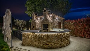Un bâtiment en pierre avec un banc circulaire en pierre devant, entouré d’une clôture et d’arbres.