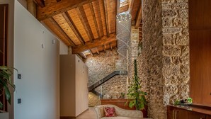 Une pièce avec un mur en pierre, des poutres apparentes en bois au plafond, un canapé blanc et un escalier menant à un niveau supérieur.