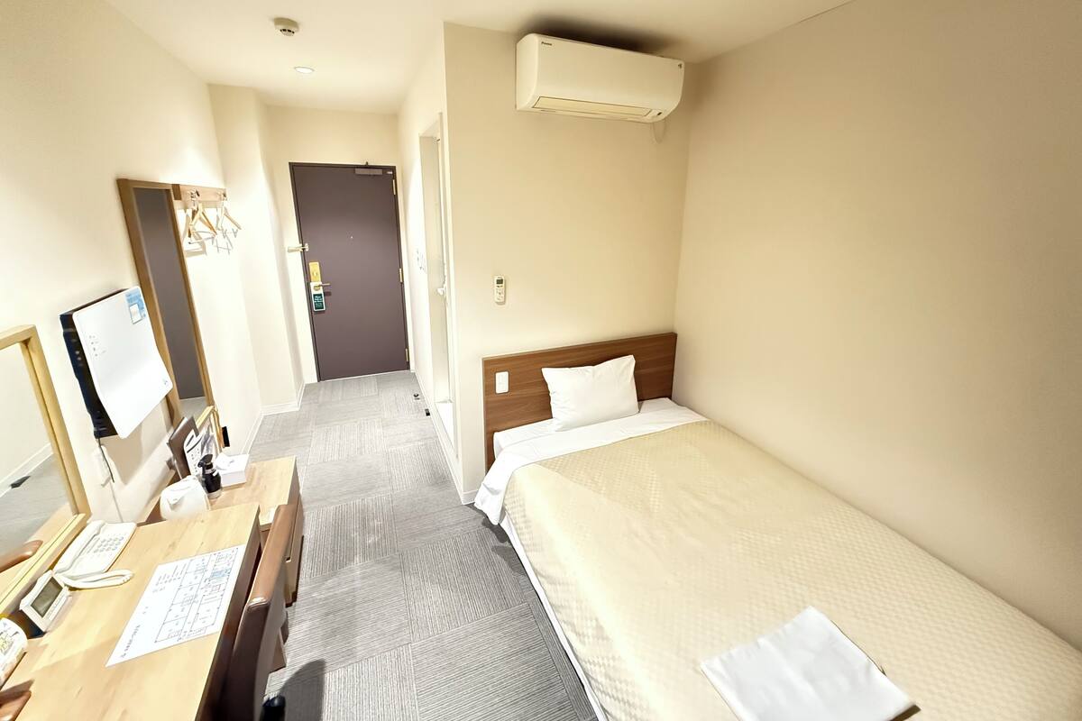Habitación de hotel con cama, escritorio con teléfono, espejo y unidad de aire acondicionado.
