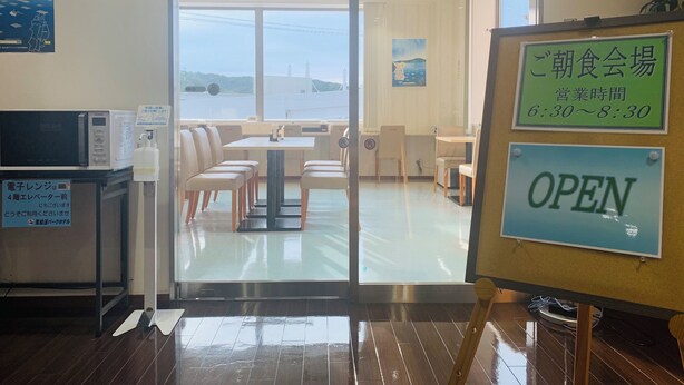 A restaurant with a glass door entrance, indoor seating, and a sign indicating operating hours. - Kesennuma Park Hotel - Adults Only (Kesennuma)
