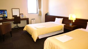 A hotel room with two beds, a desk with a computer, a chair, and a window with curtains.