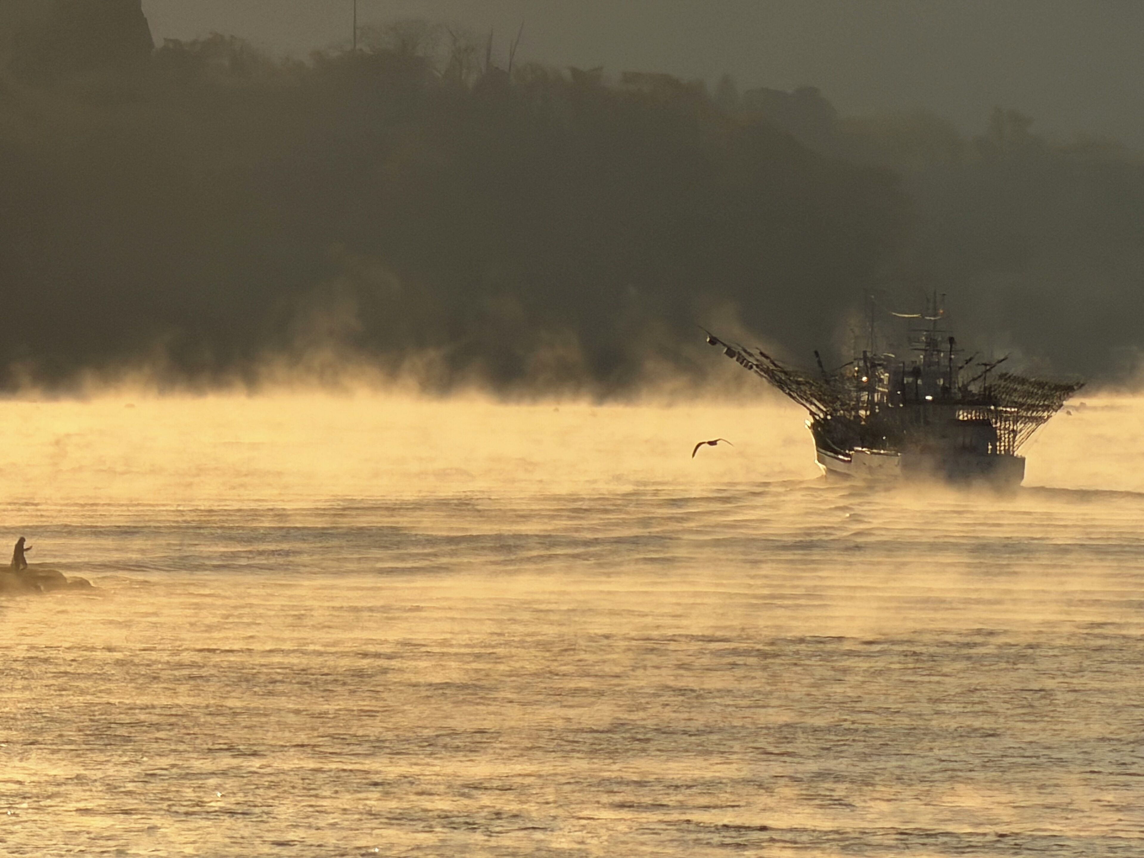 A ship in a misty harbor with calm waters and a distant shoreline.