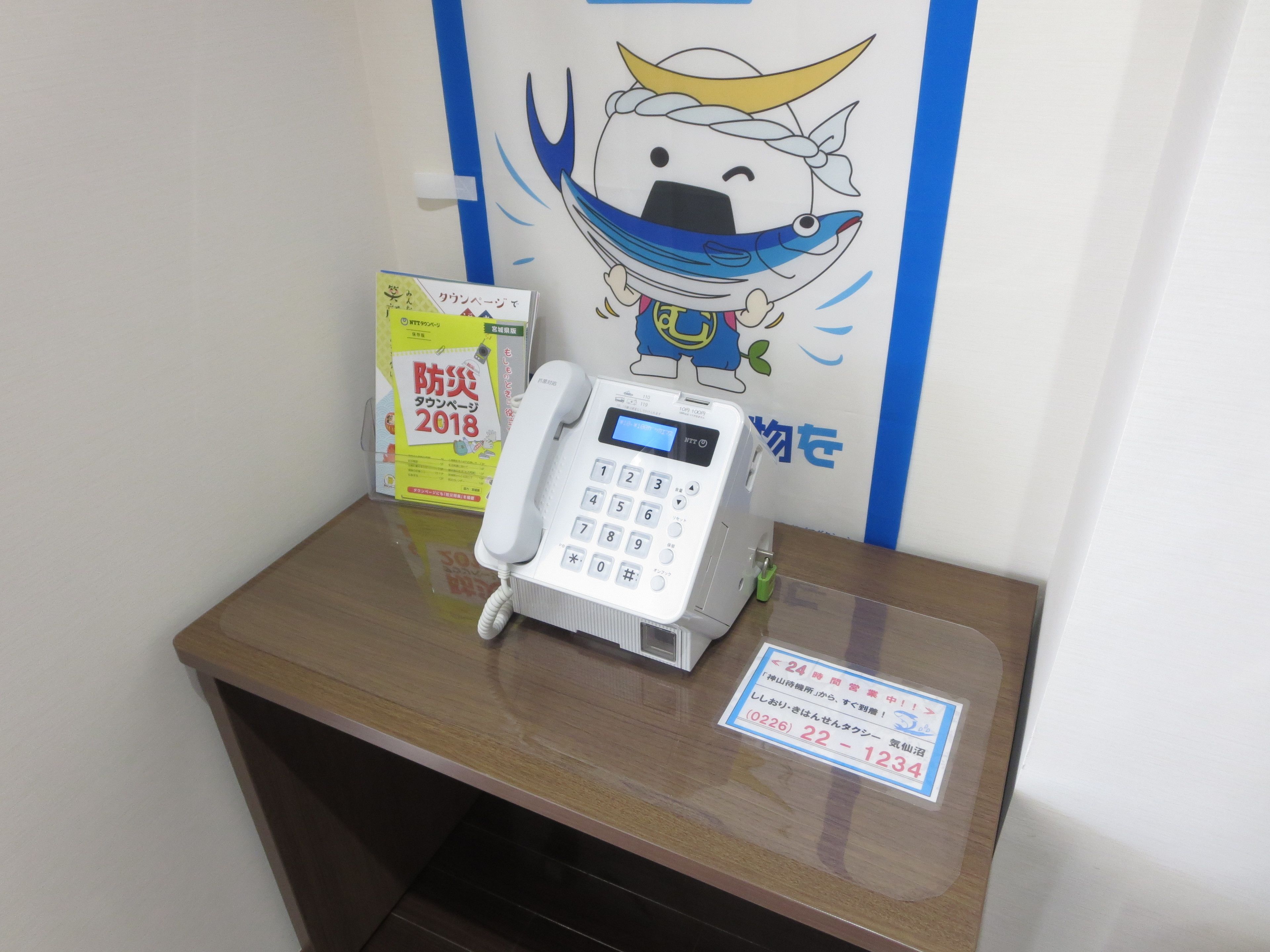 Una reception con una scrivania, un telefono, un cartello con un numero di telefono e un poster con un personaggio dei cartoni animati.
