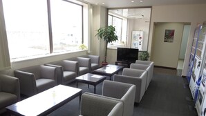 A modern waiting area with grey upholstered chairs, a flat-screen TV, and a vending machine.