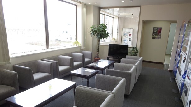 A modern waiting area with grey upholstered chairs, a flat-screen TV, and a vending machine. - Kesennuma Park Hotel - Adults Only (Kesennuma)